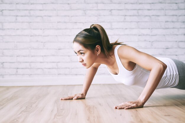 Young lady doing push-ups on the floor at home with loft design