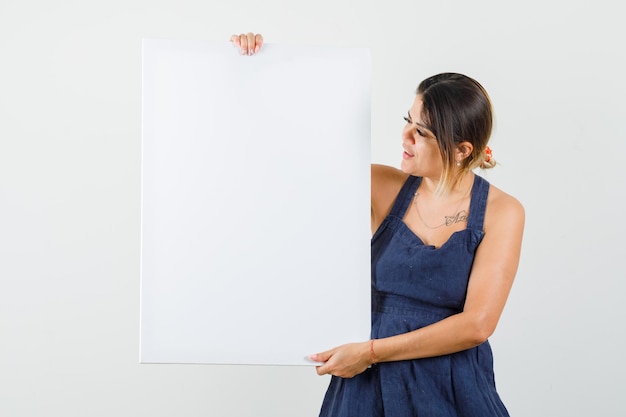 Young lady in dress holding blank canvas and looking focused