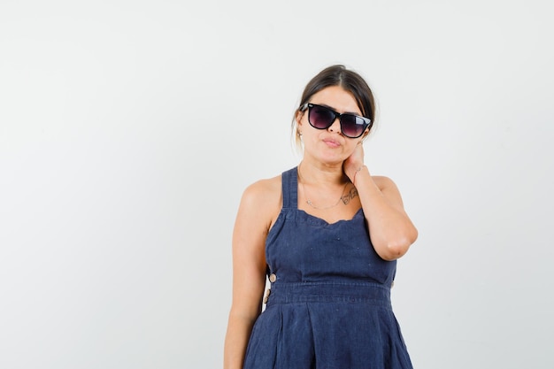 Young lady in dress holding hand on neck and looking fascinating