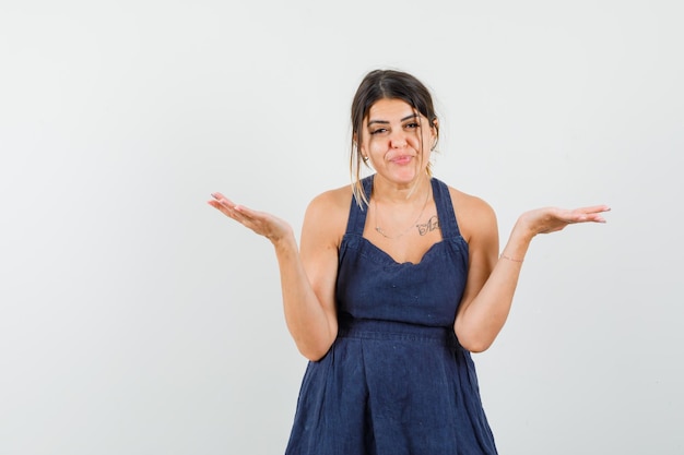 Young lady in dress showing helpless gesture and looking confused