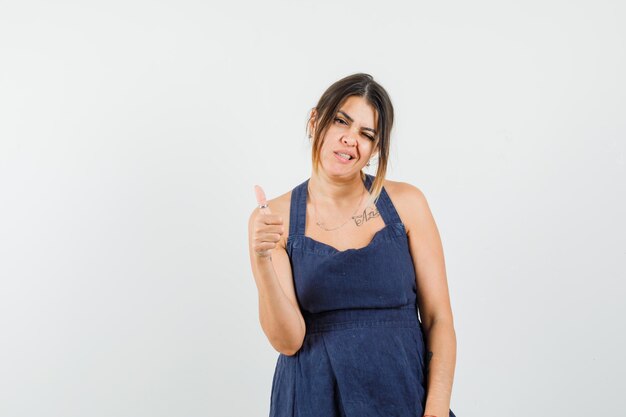 Young lady in dress showing thumb up, winking eye