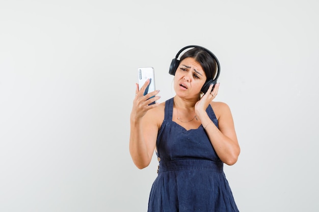 Young lady in dress taking selfie, enjoying music with headphones