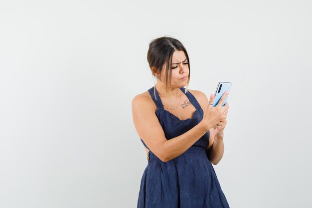 Young lady in dress using mobile phone and looking busy