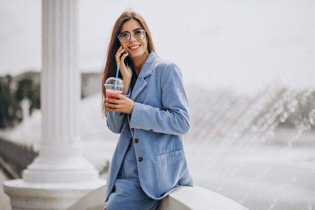 Young lady drinking ice tea in park and talking on the phone