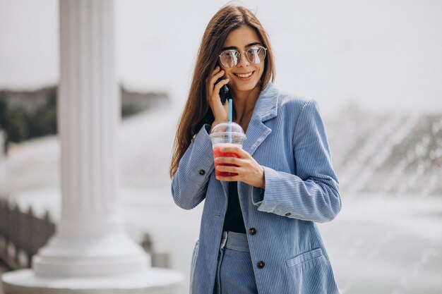 Young lady drinking ice tea in park and talking on the phone