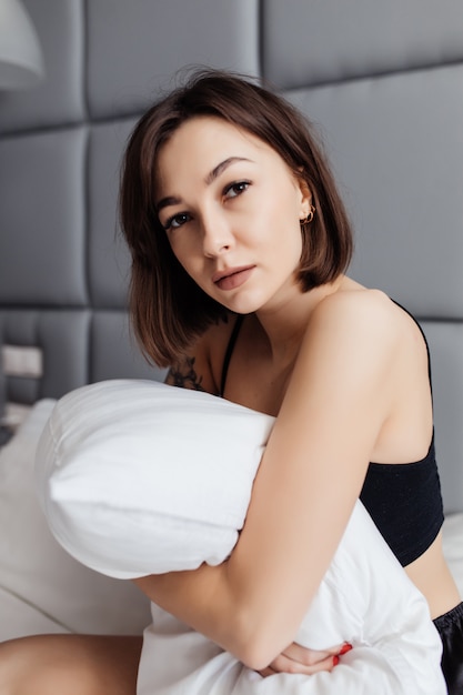 Young lady embracing her pillow in the morning in her bedroom at home