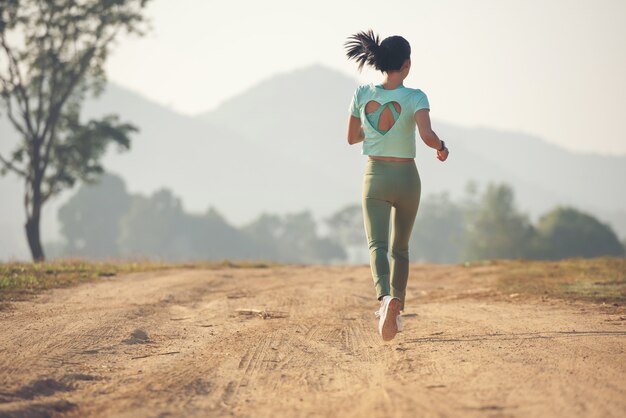 田舎道をジョギングしながら健康的なライフスタイルを楽しんでいる若い女性、屋外での運動、フィットネス、トレーニング。日没時に田舎道を走る若い女性。