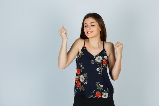 Young lady in floral top holding fists near face and looking satisfied