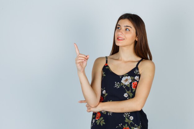 Young lady in floral top pointing up and looking wistful