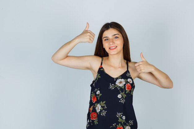 Young lady in floral top showing thumbs up and looking cheerful
