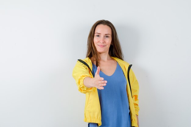 Young lady giving hand for shaking in t-shirt and looking gentle. front view.