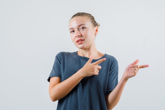 銃のジェスチャーで横を指して陽気に見える灰色のTシャツの若い女性