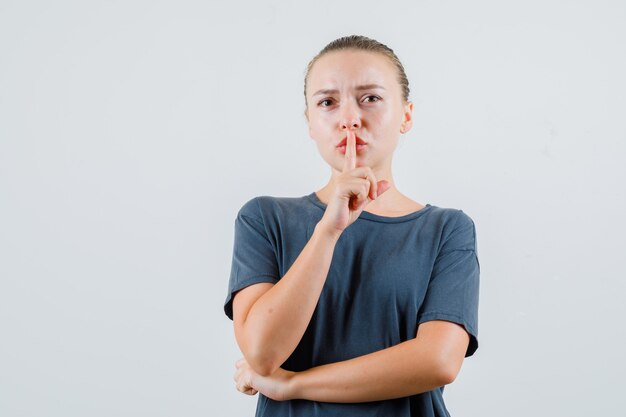 Young lady in gray t-shirt showing silence gesture and looking careful