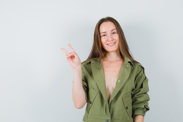 Young lady in green jacket showing victory gesture and looking confident  