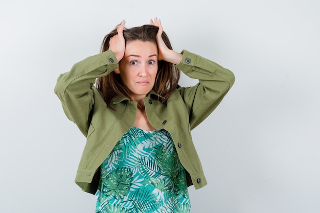 Free photo young lady in green jacket with hands on head and looking perplexed , front view.