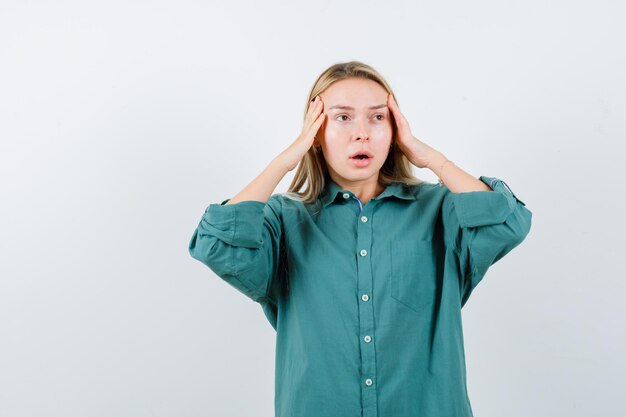 Young lady in green shirt holding hands on temples and looking helpless