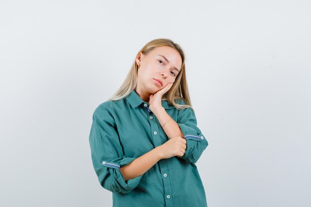 Young lady in green shirt leaning cheek on palm and looking pretty