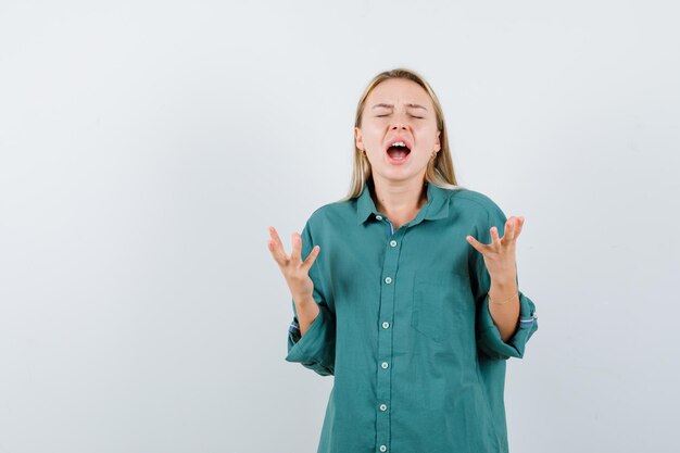 Young lady in green shirt raising hands in aggressive manner and looking wistful