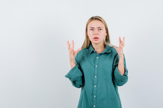 Young lady in green shirt raising hands and looking agitated