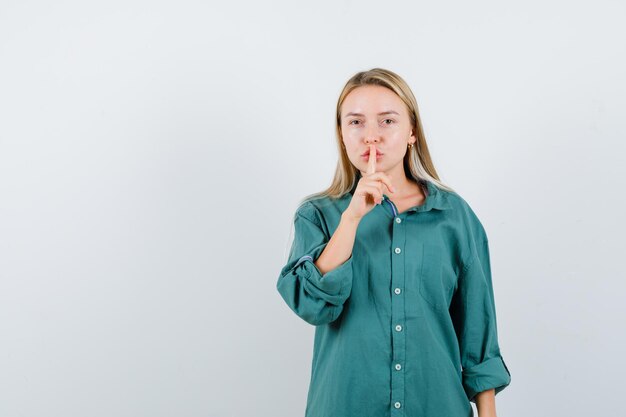 沈黙のジェスチャーを示し、自信を持って見える緑色のシャツの若い女性