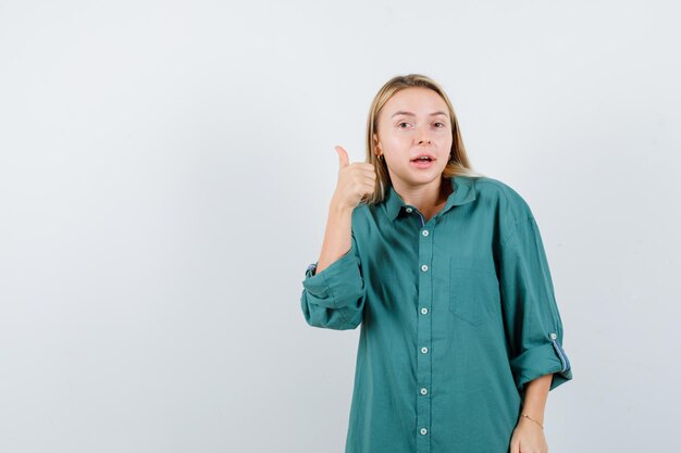 Young lady in green shirt showing thumb up and looking confident