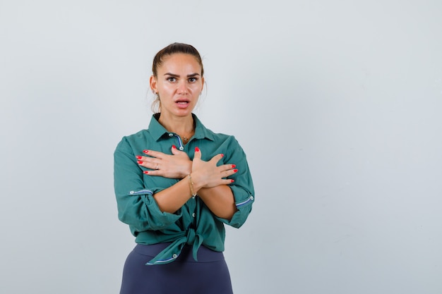 Giovane donna in camicia verde con le mani incrociate sul petto e dall'aspetto spaventato, vista frontale.