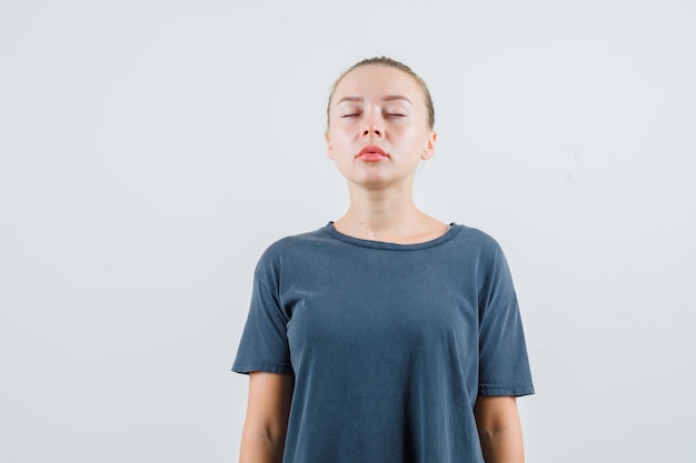 目を閉じて平和に見える灰色のTシャツの若い女性