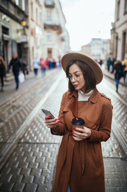 若い女性はビデオ通話をしていて、街の屋外を歩きながらコーヒーを飲む