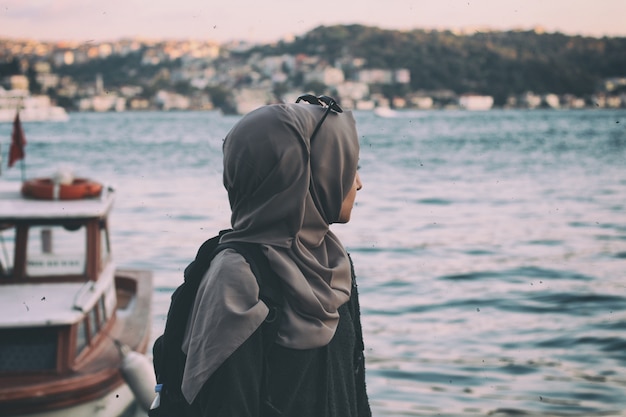 海辺のサエを見ているヒジャーブの若い女性。