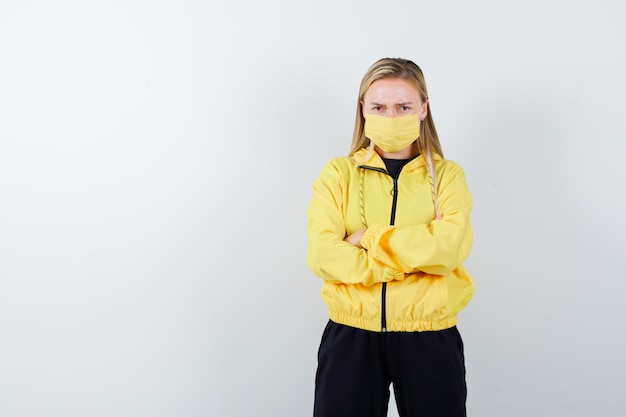 Free photo young lady holding arms folded in tracksuit, mask and looking nervous , front view.