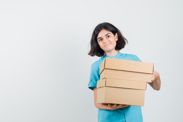 Young lady holding boxes in blue shirt and looking satisfied.