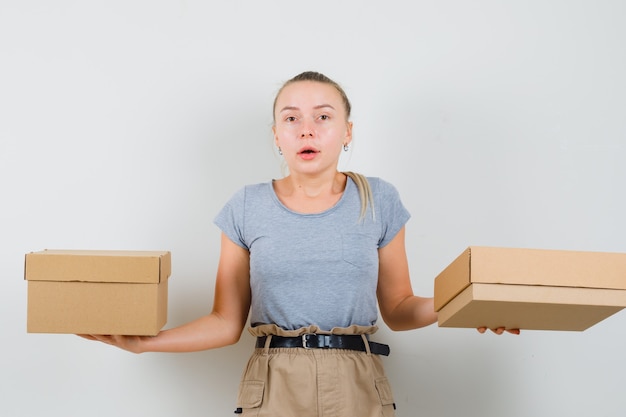 Free photo young lady holding cardboard boxes in t-shirt, pants and looking confused , front view.