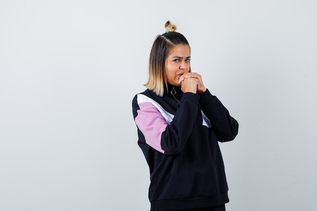 Young lady holding clasped hands on chin in hoodie sweater and looking focused.