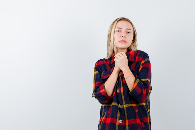 Young lady holding clasped hands to pray in checked shirt and looking peaceful , front view.