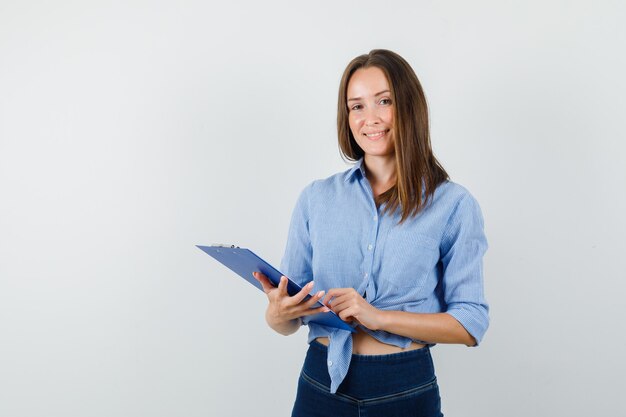 Young lady holding clipboard in blue shirt, pants and looking joyful