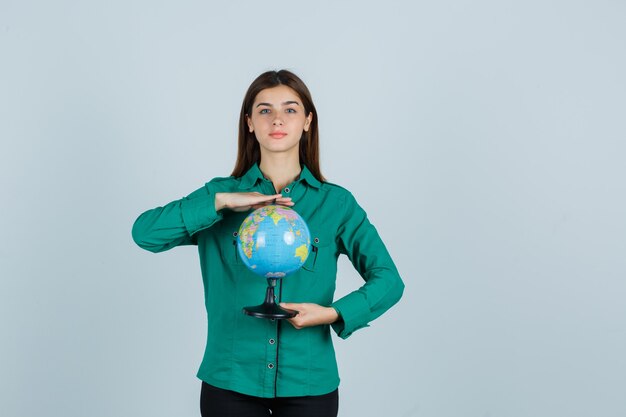 Young lady holding earth globe in shirt and looking confident. front view.