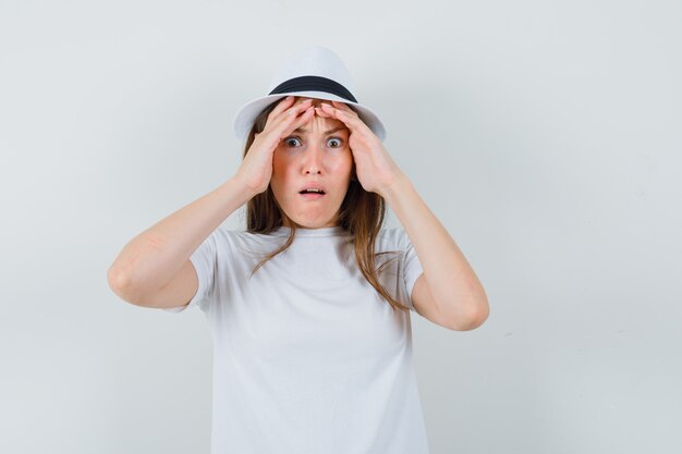 Young lady holding face with hands in white t-shirt hat and looking wistful 