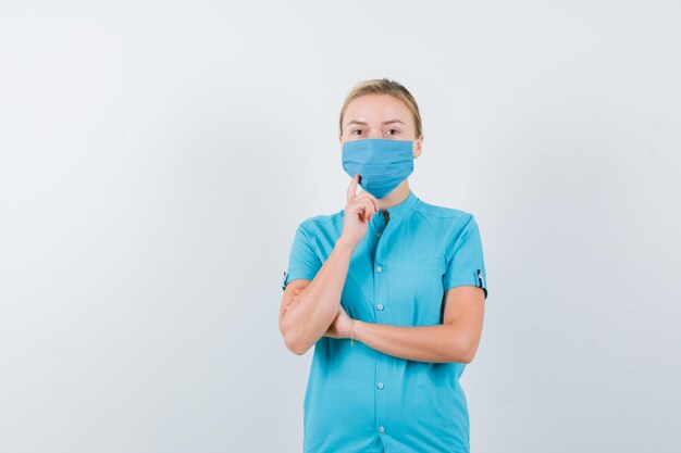 Young lady holding finger on chin in t-shirt, mask and looking confident