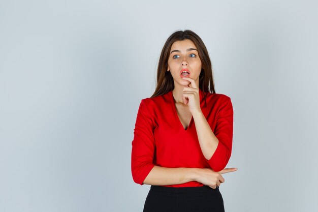 young lady holding finger on lip in red blouse, skirt and looking puzzled