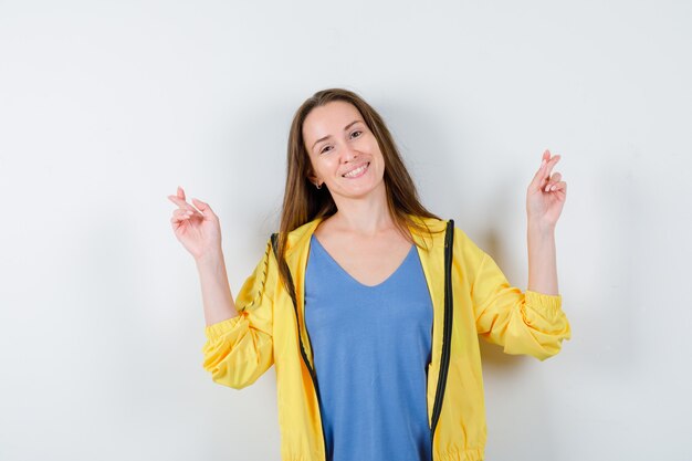 Young lady holding fingers crossed in t-shirt and looking cheerful , front view.