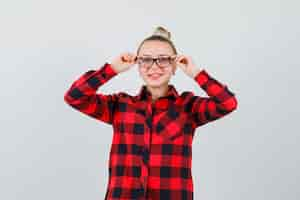 Free photo young lady holding fingers on her glasses in checked shirt and looking jolly. front view.