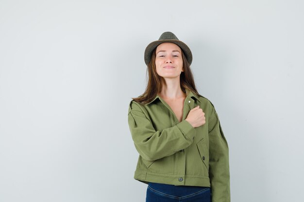 Young lady holding fist on chest in jacket pants hat and looking confident 