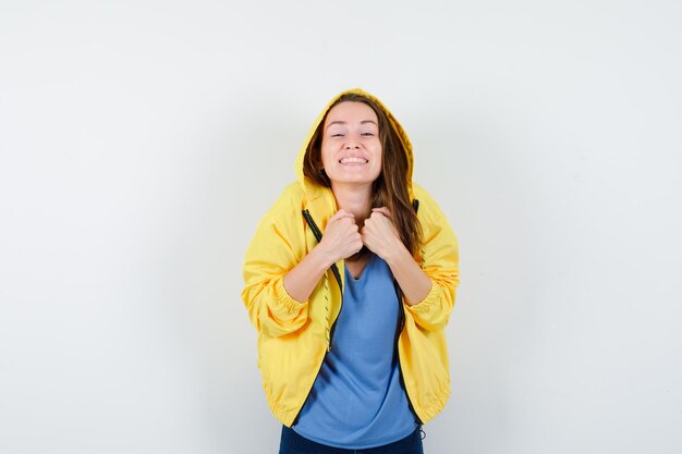 Young lady holding fists on chest in t-shirt, jacket and looking jolly