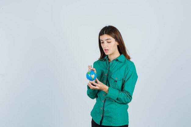 Young lady holding globe and pointing on it in shirt and looking focused. front view.