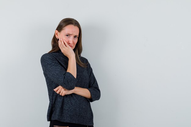 Young lady holding hand on cheek in casual shirt and looking offended. front view.