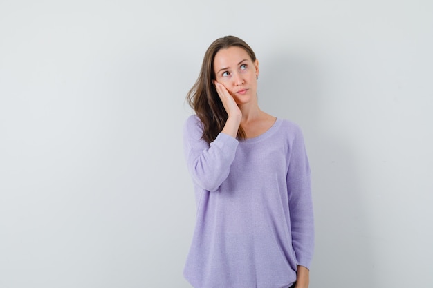 Young lady holding hand on cheek in casual shirt and looking sensible 