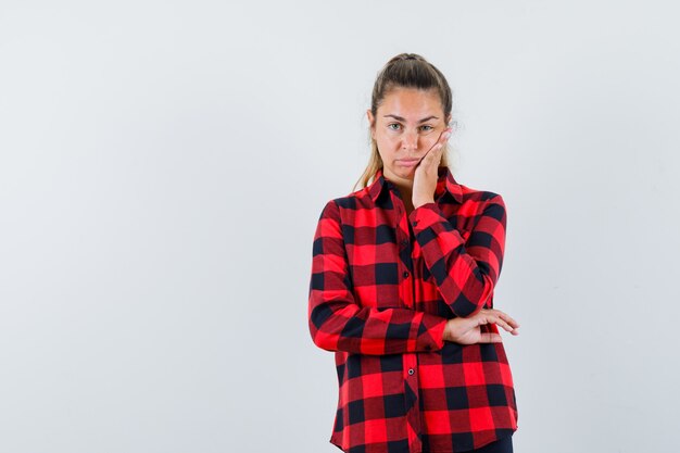 Young lady holding hand on cheek in checked shirt and looking hopeless