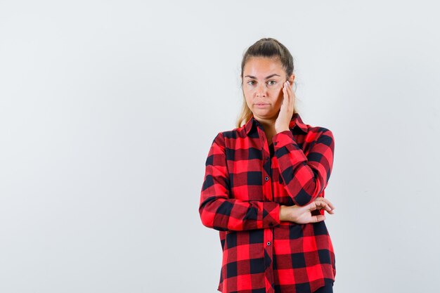 Young lady holding hand on cheek in checked shirt and looking sensible