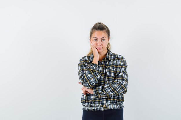 シャツ、ショートパンツ、物思いにふける、正面図で頬に手をつないでいる若い女性。
