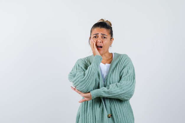 Young lady holding hand on cheek in t-shirt, jacket and looking forgetful